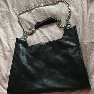 Svart axelväska med kedja - Snygg svart axelväska i skinnimitation med en kedja som axelrem. Den är stilren och stor nog att agera skolväska/arbetsväska. Aldrig använd🩷