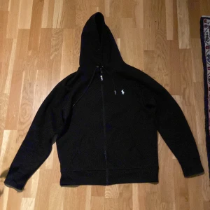 Svart hoodie från Ralph Lauren - Säljer en stilren svart hoodie från Ralph Lauren med dragkedja och det klassiska logotypbroderiet på bröstet. Perfekt för en avslappnad look. 🖤