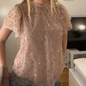 Beige/rosa glittrig blus - Säljer en elegant beige/rosa blus med glittriga paljetter. Blusen har korta ärmar och en luftig passform, perfekt för en festlig kväll eller om man vill känna sig lite extra fin till vardags.💕💕Den är tillverkad i ett lätt och bekvämt material som ger en lyxig känsla. Tröjan är från Lindex i storlek. S💕💕