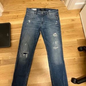 Replay Anbass Jeans - Säljer ett par snygga blå jeans från Replay, modell Anbass. De har en slim passform och är dekorerade med slitningar för en trendig look. Jeansen har klassiska fem fickor och en dragkedja. Perfekta för en avslappnad stil. Skick 9/10 Slimfit Anbass