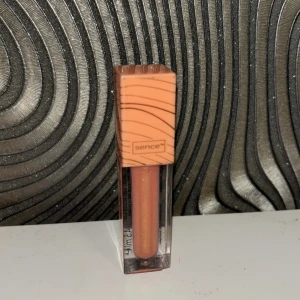 Läppglans från Sence - Snyggt läppglans från Sence i en persikofärgad nyans. Förpackningen har en stilren design med ett fyrkantigt lock i matchande färg. Perfekt för att ge läpparna en glansig finish. Luktar väldigt gott, aldrig använd!