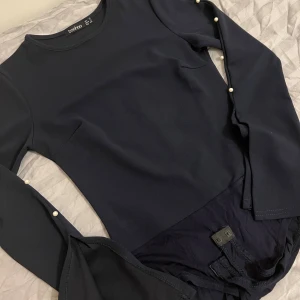 Mörkblåa bodysuit med pärlor  - Elegant mörkblå långärmad bodysuit med pärlor längs ärmarna. Den har en rund hals och en öppning i slutet på ärmarna. Aldrig använt. 