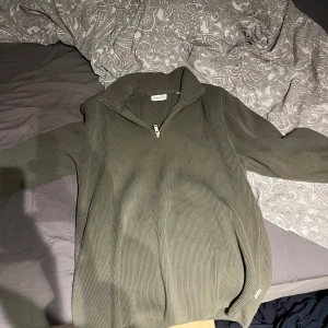 Olivgrön ribbad tröja med dragkedja - Säljer en olivgrön ribbad tröja med dragkedja. Tröjan har långa ärmar och en hög krage som kan justeras med dragkedjan. Perfekt för kyligare dagar. Storlek xl men passa L/M