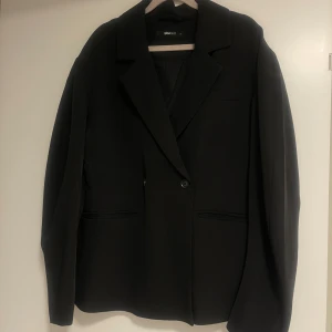 Svart figurnära kavaj från Gina Tricot - Snygg svart kavaj från Gina Tricot i storlek S. Kavajen har en klassisk design med knappar framtill och är perfekt för en stilren look. Passar utmärkt till både vardag och fest.