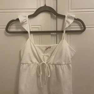 Vit linnetopp från Nelly(storlek s) - Säljer en söt vit linnetopp från Nelly med volangdetaljer på axelbanden och knytning framtill. Perfekt till vår och sommar
