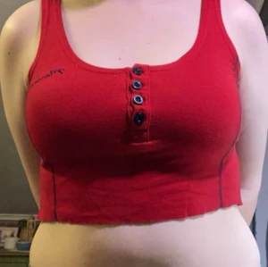 Röd croppad linnetopp - Säljer en röd croppad linnetopp med knappar framtill. Toppen har en enkel design med breda axelband. Storlek s men stretchig och passar större.