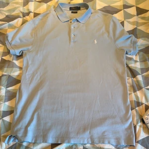 Ljusblå pikétröja från Ralph Lauren - Säljer en stilren ljusblå pikétröja från Ralph Lauren. Tröjan har en klassisk krage och knappar framtill. Den är i slim fit och tillverkad i stretchigt material för extra komfort. Perfekt för en avslappnad men ändå snygg look. Perfekt till sommaren. 