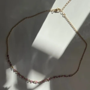 Guldhalsband med lila pärlor - Elegant guldhalsband med små lila pärlor. Perfekt för att ge en färgklick till din outfit. Kedjan är tunn och smidig med ett klassiskt lås.