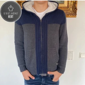 Grå och blå stickad hoodie - Säljer en grå och blå stickad hoodie från. Den har en dragkedja framtill och en mysig fodrad huva. Två praktiska fickor på framsidan och ribbade muddar vid ärmslut och nederkant. Perfekt för kyliga dagar!