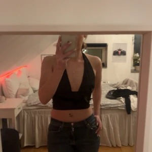 Svart halterneck topp - Snygg svart halterneck topp med djup urringning. Perfekt för en kväll ute eller en somrig dag. Toppen är ärmlös och har en tight passform som framhäver figuren. 