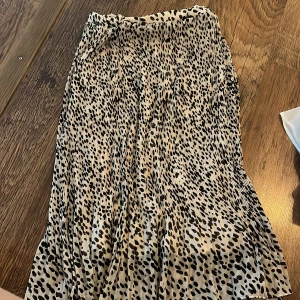 Prickig kjol från Pieces - Säljer en superfin prickig kjol från Pieces. Den är i en beige och svart färgkombination med ett coolt prickigt mönster. Kjolen är plisserad och har en elastisk midja för extra komfort. Perfekt för både vardag och fest! 🖤obs! Kjolens resor i midjan är lite korvad. 