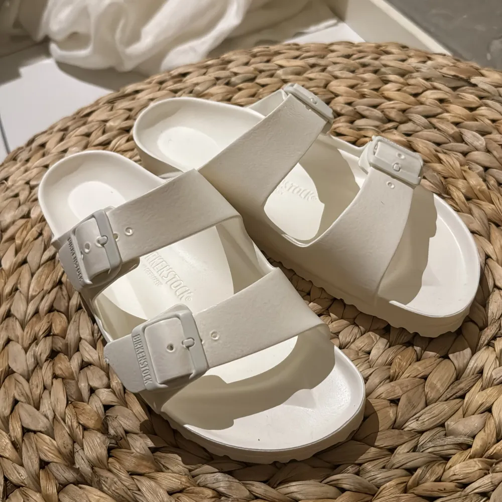 Säljer ett par vita sandaler från Birkenstock i syntetmaterial. De har två justerbara remmar med spännen för perfekt passform. Perfekta för sommardagar och ger en skön komfort hela dagen. Passar både till stranden och stan!. Skor.