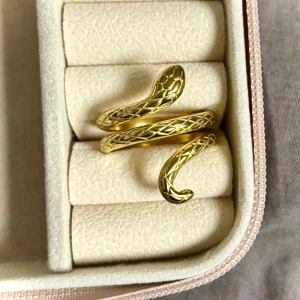 Guldfärgad ormring - Snygg och unik guldfärgad ring formad som en orm. Den har ett detaljerat mönster som liknar ormskinn och är perfekt för att ge en edgy touch till din outfit. Ringen är justerbar och passar de flesta storlekar. Perfekt accessoar för både vardag och fest!