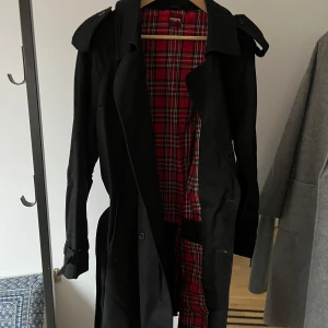Trenchcoat herr från Merc London - Jättefin trenchcoat med klassisk rördrutigt tyg på insidan som Merc London brukar har. Googla gärna. Nypris på deras kappor är 120-270 pund. Detta är ett kap. Den har två praktiska innerfickor på vänster sida. Bomullsaktigt tyg på både in- och utsida. En knapp lite lös. Lätt att sy fast bättre så att den sitter på plats. 