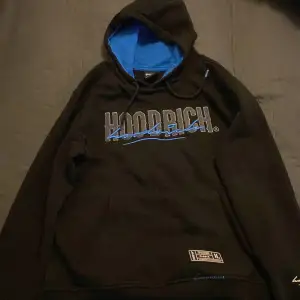 Säljer en svart hoodie från Hoodrich med blå detaljer och texten 'FROM NOTHING TO SOMETHING'. Den har en stor luva med blått foder och en bekväm passform. Perfekt för höst och vinter!