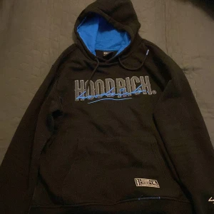 Svart hoodie från Hoodrich - Säljer en svart hoodie från Hoodrich med blå detaljer och texten 'FROM NOTHING TO SOMETHING'. Den har en stor luva med blått foder och en bekväm passform. Perfekt för höst och vinter!