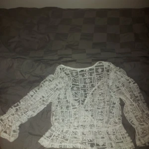 Vit spetsblus från Zara - Säljer en superfin vit spetsblus från Zara i storlek M. Blusen har ett vackert spetsmönster och långa ärmar. Perfekt för både vardag och fest! Den har en omlott-design som ger en elegant touch. Använd den med ett par jeans eller en kjol för en chic look.