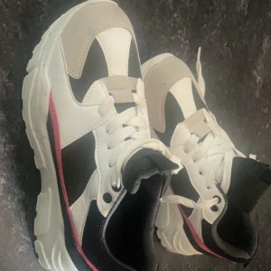 Snygga sneakers från Raxmax - Säljer ett par coola sneakers från Raxmax i mycket bra skick. De har en stilren design med vita, svarta och beige paneler samt en röd detalj på sidan. Perfekta för både vardag och träning!