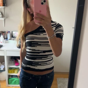 Svartvit randig oneshoulder-topp - Säljer en snygg svartvit randig oneshoulder-topp. Den har en tight passform och är perfekt för både vardag och fest. Materialet är mjukt och stretchigt, vilket gör den bekväm att bära hela dagen. Passar perfekt till jeans eller kjol för en stilren look.