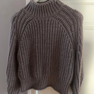 Brun stickad tröja från H&M - Mysig brun stickad tröja från H&M i storlek S. Perfekt för kyliga dagar med sin tjocka och varma design. Tröjan har en hög krage och långa ärmar, vilket gör den idealisk för höst och vinter. Den ribbade strukturen ger en snygg och trendig look!