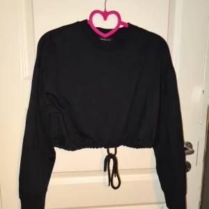 Svart croppad tröja från Even&Odd - Säljer en svart croppad tröja från Even&Odd. Den har långa ärmar och en snygg knytning i midjan som ger en cool look. Perfekt för både vardag och fest! 🖤