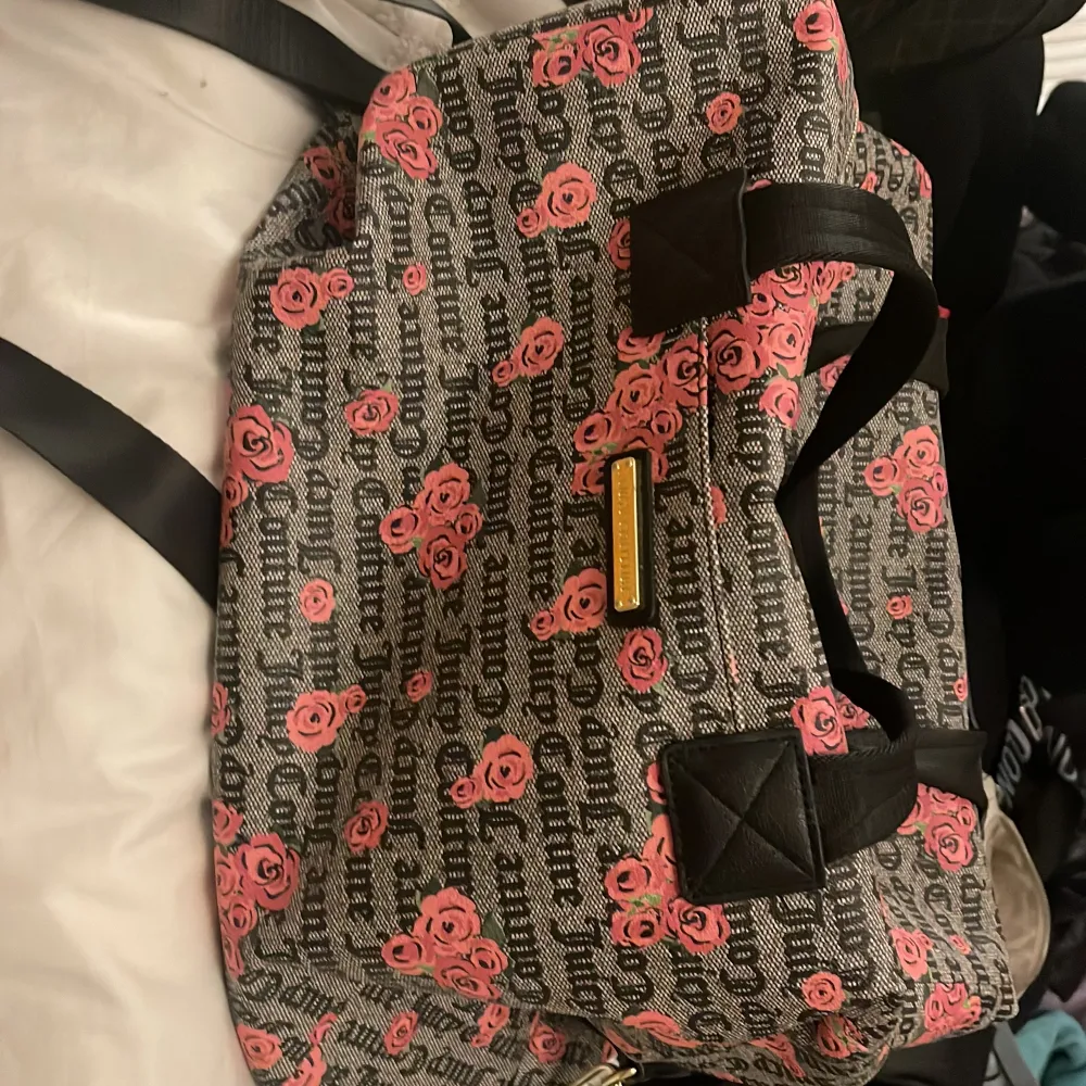 Säljer en snygg Juicy Couture väska med ett coolt mönster av rosa rosor och text. Väskan har svarta handtag och en guldig logga framtill. Perfekt för att ge din outfit en extra touch! 👜. Väskor.