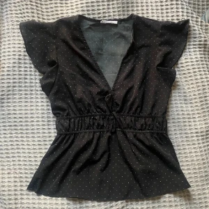 Svart blus med prickigt mönster - Säljer en söt svart blus med små vita prickar. Den har en v-ringad design och korta ärmar med en elastisk midja som ger en fin passform❤️Första bilden är lånad av tjejen jag köpte från!