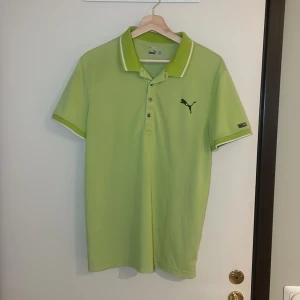 Grön pikétröja från Puma - Säljer en fräsch grön pikétröja från Puma i sportig polyester. Den har en klassisk krage med knappar och det ikoniska Puma-loggan på bröstet. Perfekt för både träning och vardag. Skön och luftig passform! Pris går alltid att förhandlas! 