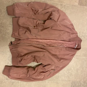 Rosa bomberjacka från Frankie Shop - Säljer en snygg gammelrosa bomberjacka  i storlek M. Jackan har en dragkedja framtill och en praktisk ficka med dragkedja på ärmen. Den är perfekt för vår och höst och har en cool, avslappnad stil. Passar perfekt till både vardag och fest!