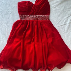 Röd klänning från Little Mistress  - Säljer en superfin röd klänning från Little Mistress köpt på Nelly i storlek XS, passar även S. Den är axelbandslös med en glittrig paljett-detalj i midjan och har en omlott-design upptill. Perfekt för fest eller nyår! 💃