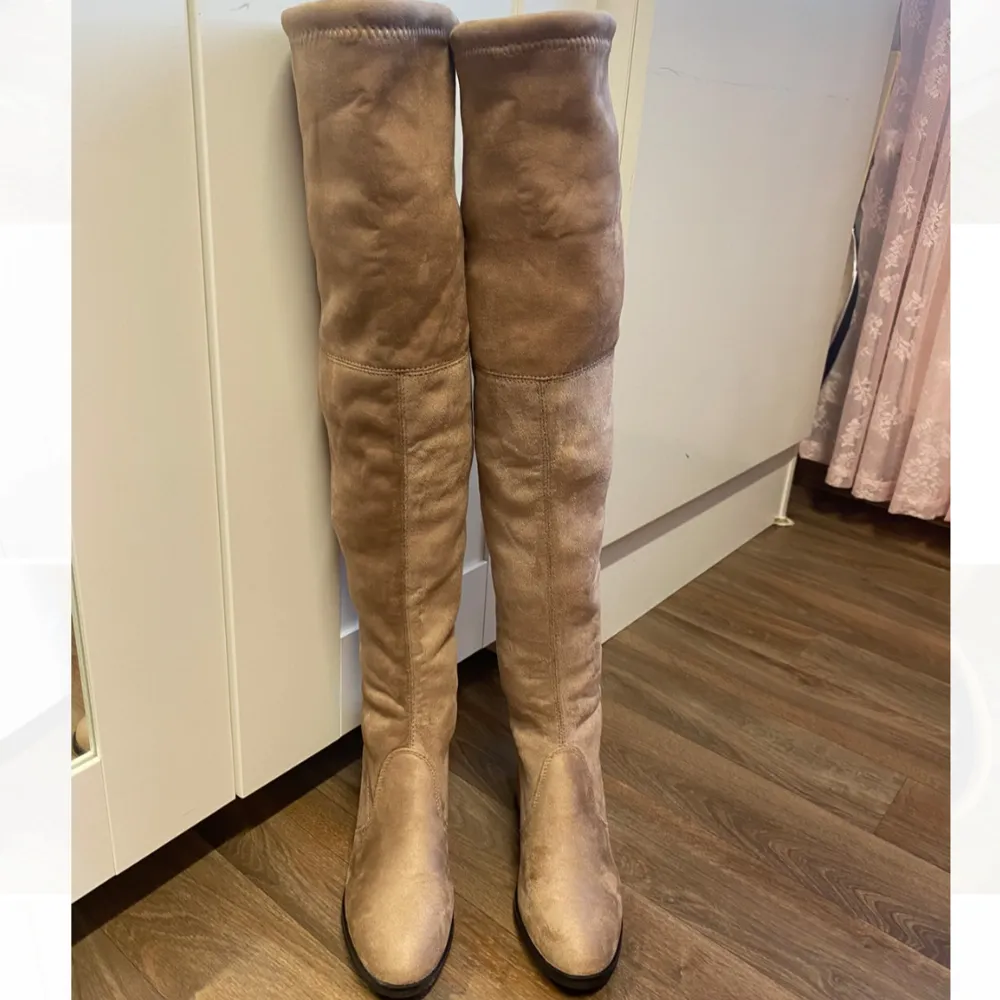 Säljer ett par nya snygga beige overknee boots. De har en stilren design med rund tå och en liten klack för extra komfort. Perfekta för höst och vinter, och de har en knytning baktill för justerbar passform. Använd dem till både vardags och fest för en chic look!. Skor.