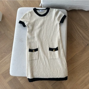 Beige stickad klänning från Zara - Säljer en superfin beige stickad klänning från Zara. Den har svarta detaljer vid ärmslut, hals och nederkant samt två fickor med dekorativa knappar. Perfekt för höst och vår! 🖤