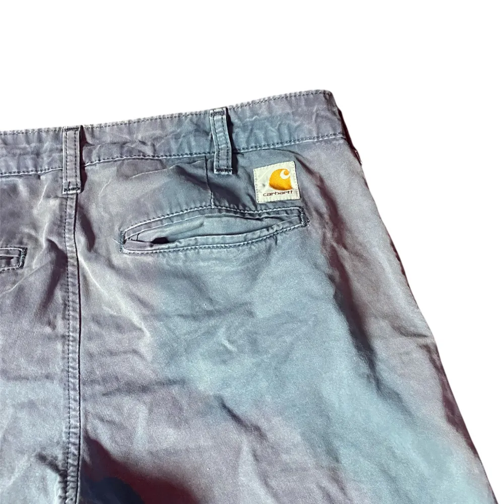 Säljer ett par grå shorts från Carhartt i bra skick. De har en klassisk design med knappar och bälteshällor. Perfekta för sommaren med en avslappnad passform. Shortsen har fickor både fram och bak, vilket gör dem praktiska för vardagsbruk.. Shorts.