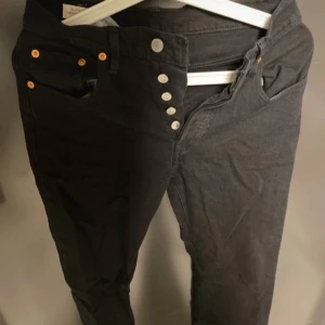 Svarta Levi's Premium jeans - Säljer ett par svarta Levi's Premium jeans i storlek W25 L28. De har en snygg knappdetalj framtill och klassiska bakfickor. Perfekta för både vardag och fest! 🖤