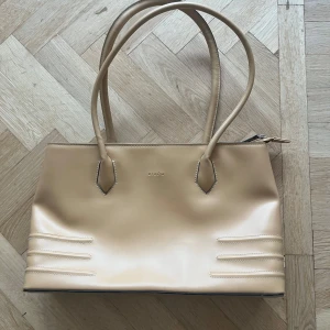 Beige/gul axelväska  - Snygg beige/gul axelväska i syntetmaterial. Väskan har en stilren design med dragkedja upptill och flera fack inuti för smart förvaring. Perfekt för både vardag och fest! 👜✨