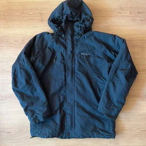 Svart jacka från Carhartt - Säljer en svart Carhartt jacka i storlek XS. Den har en praktisk huva och dragkedja framtill. Perfekt för höst och vinter med sitt slitstarka polyester material. Jackan har långa ärmar och en stilren design. Passar både till vardags och utomhusaktiviteter.