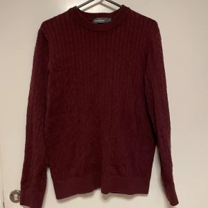 Vinröd tröja från Dressmann - Säljer en stilren vinröd tröja från Dressmann. Tröjan har ett diskret kabelstickat mönster och är långärmad med ribbade kanter vid hals, ärmslut och nederkant. Perfekt för kyligare dagar.