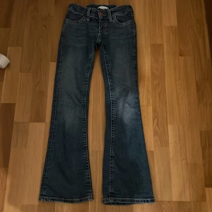 Blå bootcut jeans från Gina Tricot - Snygga blå bootcut jeans från Gina Tricot med klassisk femficksdesign. Jeansen har en lätt tvättad look och dekorativa sömmar på bakfickorna. Perfekta för en avslappnad stil.