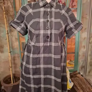Säljer en svart och vit rutig klänning med korta ärmar och knappar framtill. Klänningen har en klassisk krage och en avslappnad passform som ger en stilren look. Perfekt för en dag ute eller en avslappnad kväll.