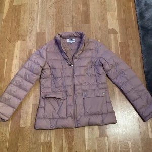 Beige dunjacka från Hampton Republic - Säljer en stilren beige dunjacka från Hampton Republic. Jackan har en dragkedja framtill och praktiska fickor med knappar. Perfekt för kyligare dagar med sin quiltade design och långa ärmar.