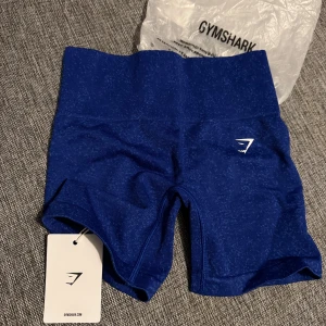 Blå shorts från Gymshark - Snygga blå shorts från Gymshark, perfekta för träning. De har en hög midja och är tillverkade i ett stretchigt material för bästa komfort. Gymshark-loggan syns diskret på sidan. Perfekta för att hålla stilen på gymmet!