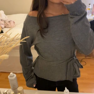 Grå offshoulder tröja med knytband - Säljer denna jätte söta unika topp med knyte. Säljer pågrund av att den inte kom till användning. Man kan välja att inte ha bandet i midjan❣️