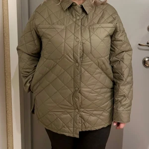 Olivgrön quiltad jacka - Snygg olivgrön quiltad vårjacka med krage och långa ärmar. Jackan har en stilren design med knappar framtill och två bröstfickor. Nytt pris  130 euro.