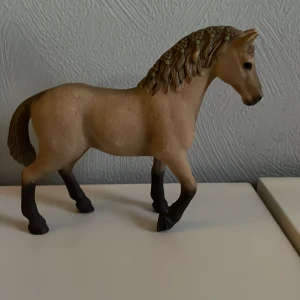 Schleich häst - Detaljerad beige hästfigur med mörkare man och svans. Perfekt för samlare eller som leksak. Hästen har en realistisk design med mörka ben och uttrycksfulla ögon.