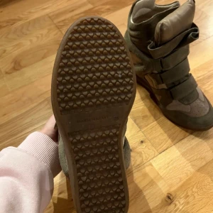 Gröna sneakers från Isabel Marant - Säljer ett par gröna sneakers från Isabel Marant med en unik design. Skorna har en kombination av mocka och syntetmaterial samt kardborreband för enkel justering. Perfekta för en stilren look.
