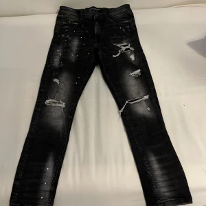 Svarta slitna jeans - Snygga svarta jeans från supply and demand i storlek 30/S med slitningar och färgstänk för en trendig look. De har en slim passform. Jeansen har klassisk femficksdesign och kedjegylf