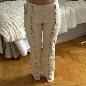 Vita byxor med snörning - Sjukt snygga naturvita byxor med unik snörning längs benen. De har en normalhög midja och en straight passform. Helt oanvända med lapparna kvar. Storlek 38 men skulle mer säga 36