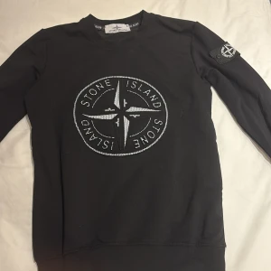 Svart långärmad tröja från Stone Island - Säljer en svart långärmad tröja från Stone Island med det ikoniska logotypmärket på bröstet och ärmen. Tröjan har en rund halsringning och är perfekt för en stilren look. Skick 10/10 inte använd.