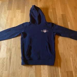 Mörkblå hoodie från GANT - Säljer en snygg mörkblå hoodie från Gant i nyskick. Skick 9.5/10 och inga defekter. Tröjan är för 10-12år och stl runt 150cm. Skicka ett meddelande ifall du har någon fundering.👍☺️😊