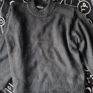 Svart stickad tröja - Säljer en klassisk svart stickad tröja med rund hals och långa ärmar. Perfekt för kyliga dagar och enkel att matcha med olika outfits. Tröjan har ribbstickade muddar vid ärmslut och nederkant. Helt ny och oanvänd!